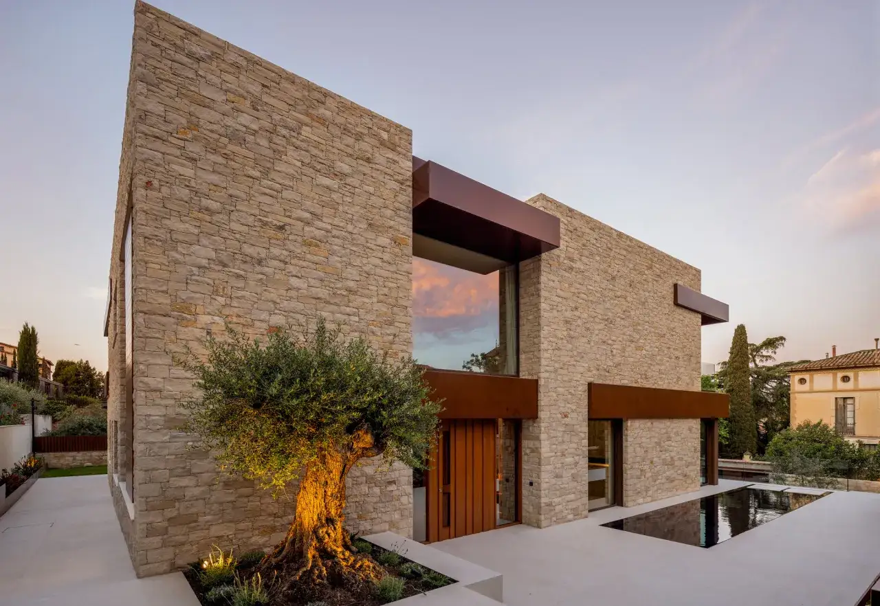Fachada casa pueblo moderna de piedra con olivo centenario y piscina.