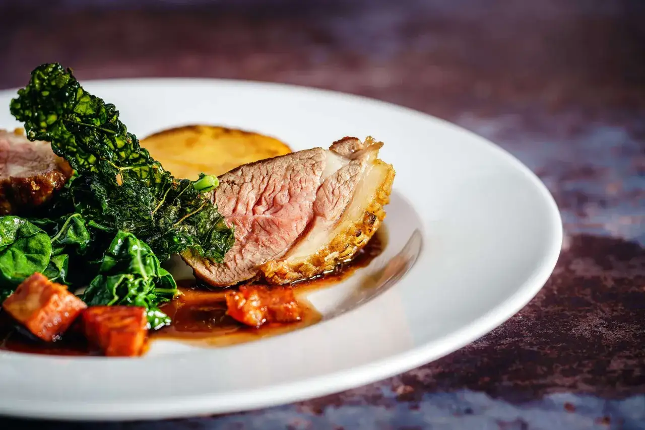 Un plat de vin avec agneau, accompagn&eacute; de l&eacute;gumes verts et de pommes de terre r&ocirc;ties.