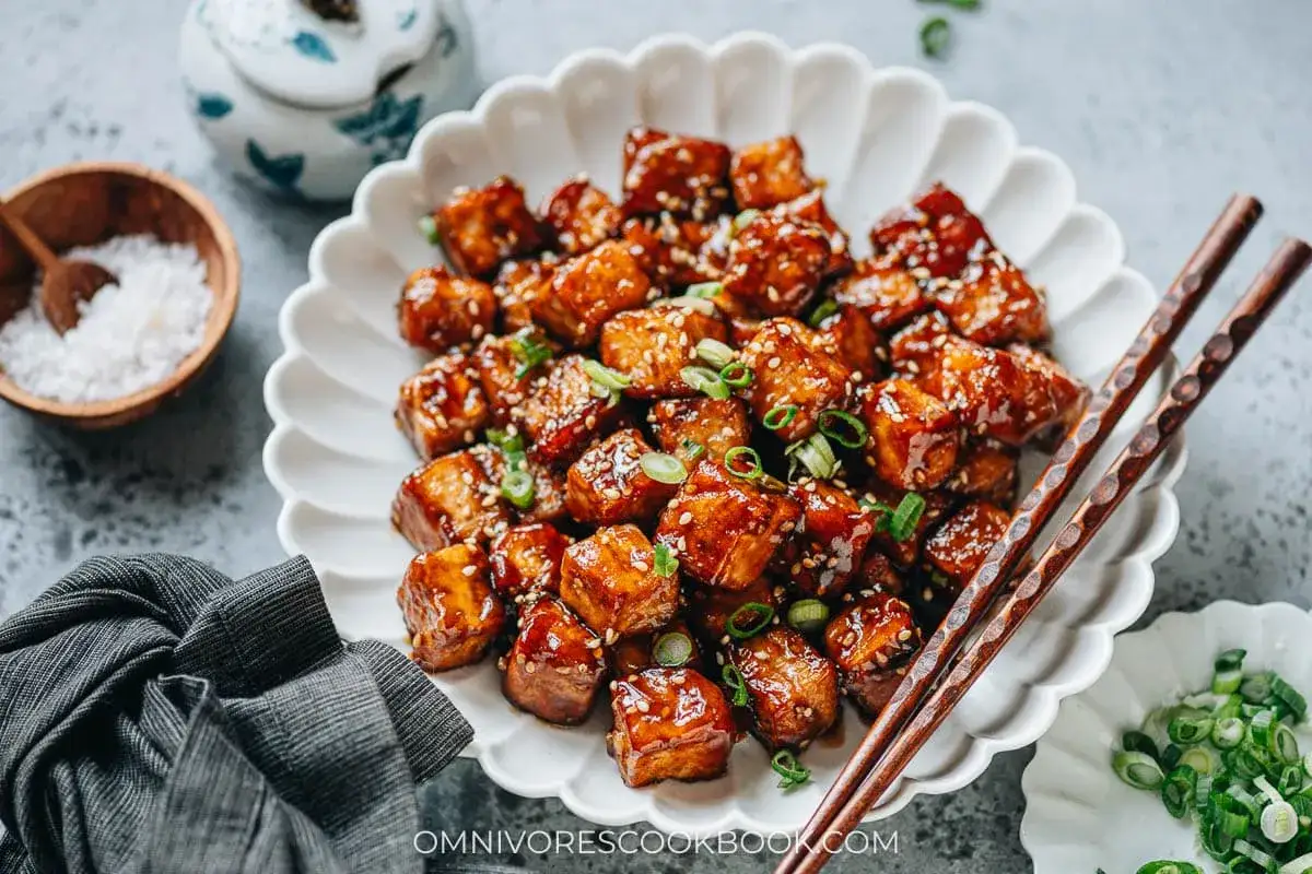 Leckeres, klebriges Tofu-Rezept mit Sesam und Frühlingszwiebeln auf einem weißen Teller, bereit zum Genießen.