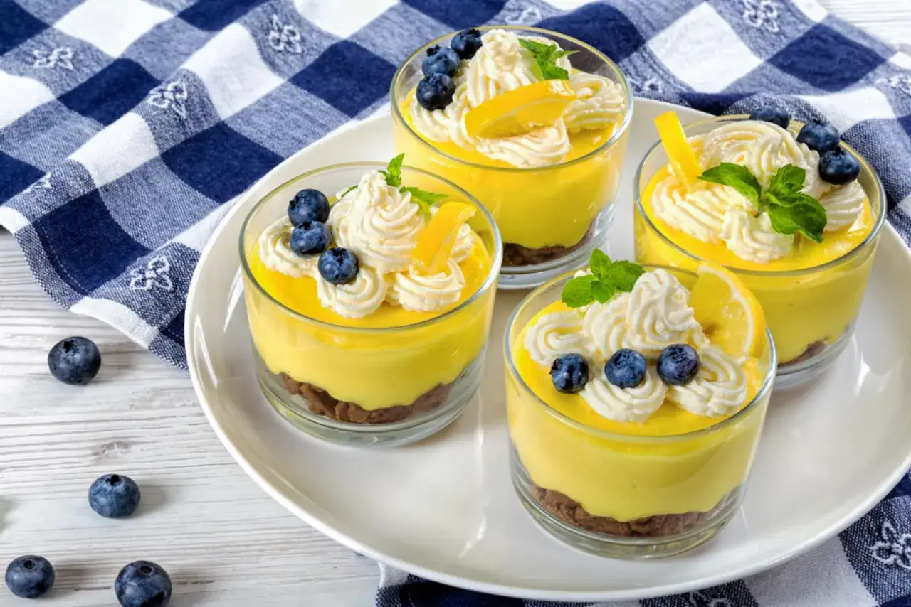 Cuatro copas de cremoso mousse de limón, decoradas con crema batida, arándanos y rodajas de limón.