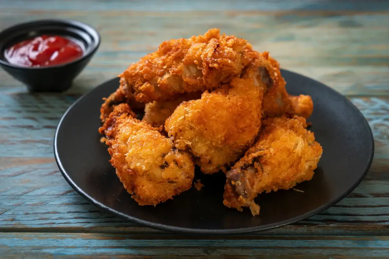 Chrupiące skrzydełka z airfryer na czarnym talerzu, obok miseczka z ketchupem. Idealna przekąska!