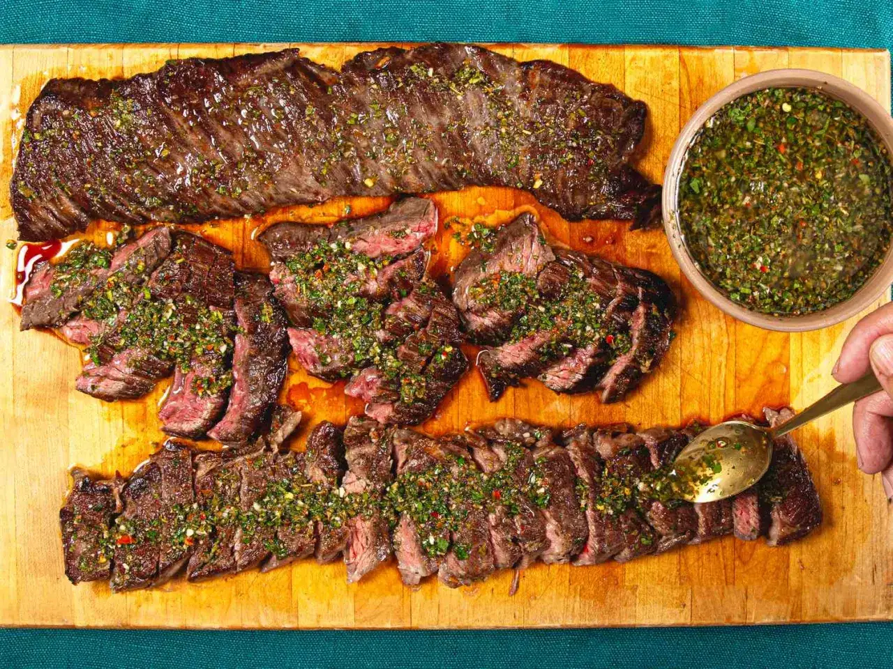 Un steak Black Angus grillé, tranché et nappé d'une sauce verte. Une cuillère sert le jus savoureux.