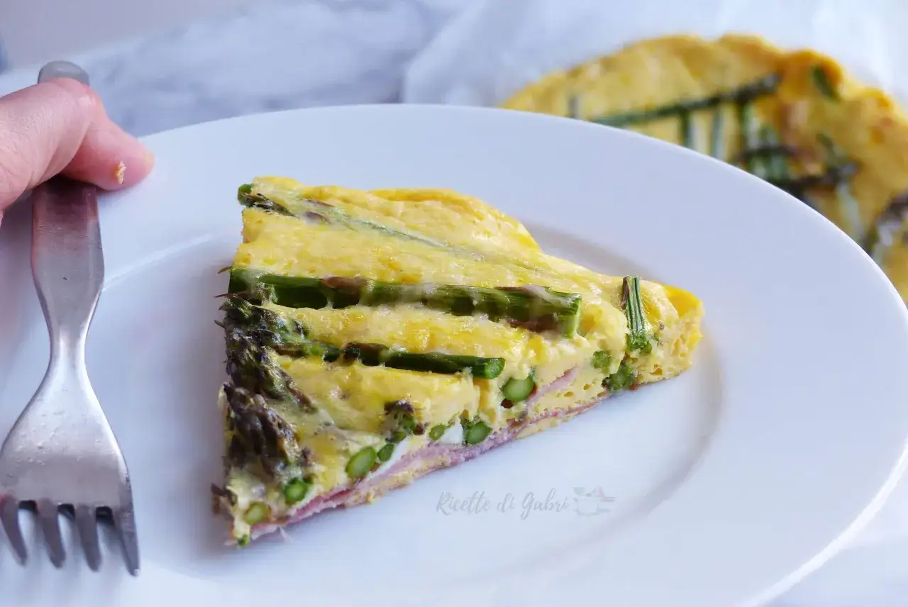 Una fetta di frittata di asparagi, con prosciutto e formaggio, su un piatto bianco, pronta per essere gustata.