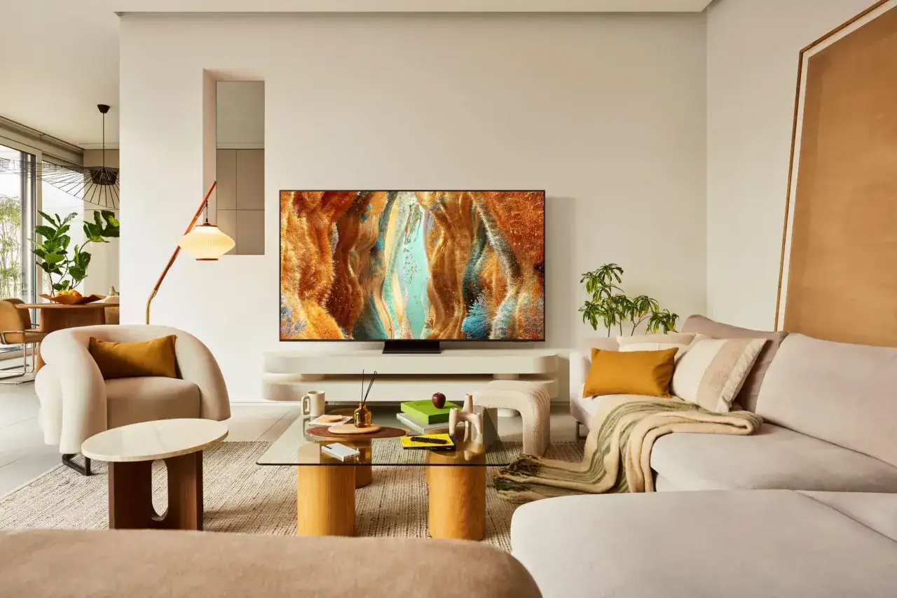Nowoczesny salon z telewizorem QLED prezentującym abstrakcyjny obraz. Miękkie meble i designerskie oświetlenie tworzą przytulną atmosferę.