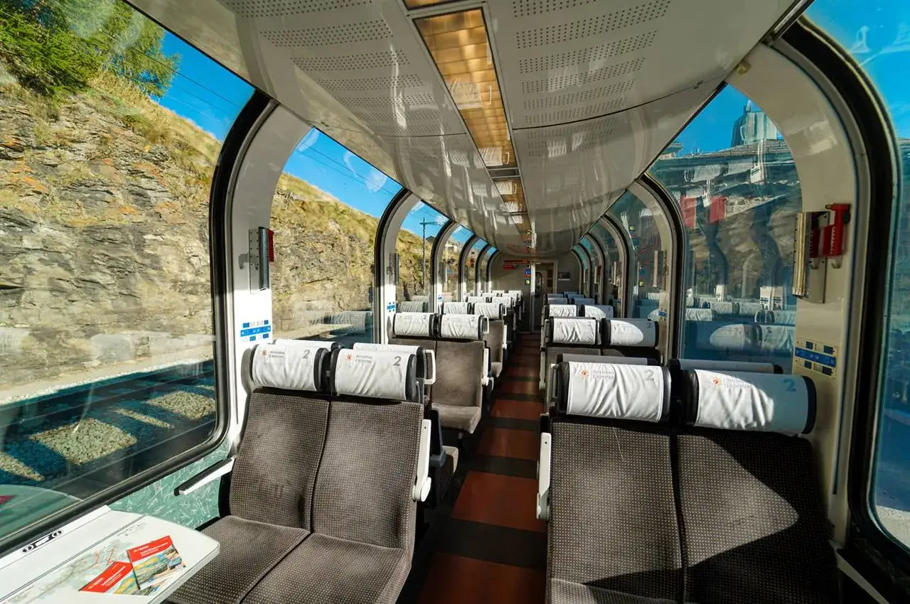 Interno del trenino del Bernina, con sedili marroni e poggiatesta bianchi, pronti per il percorso panoramico tra le montagne.