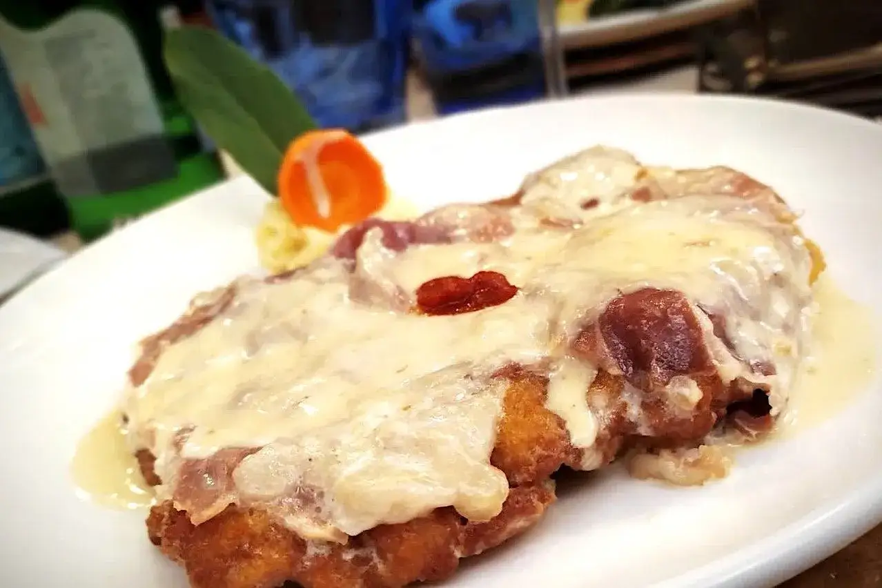 Cotoletta alla bolognese filante, con prosciutto e formaggio fuso, servita su un piatto bianco con contorno di pur&egrave; e carota.