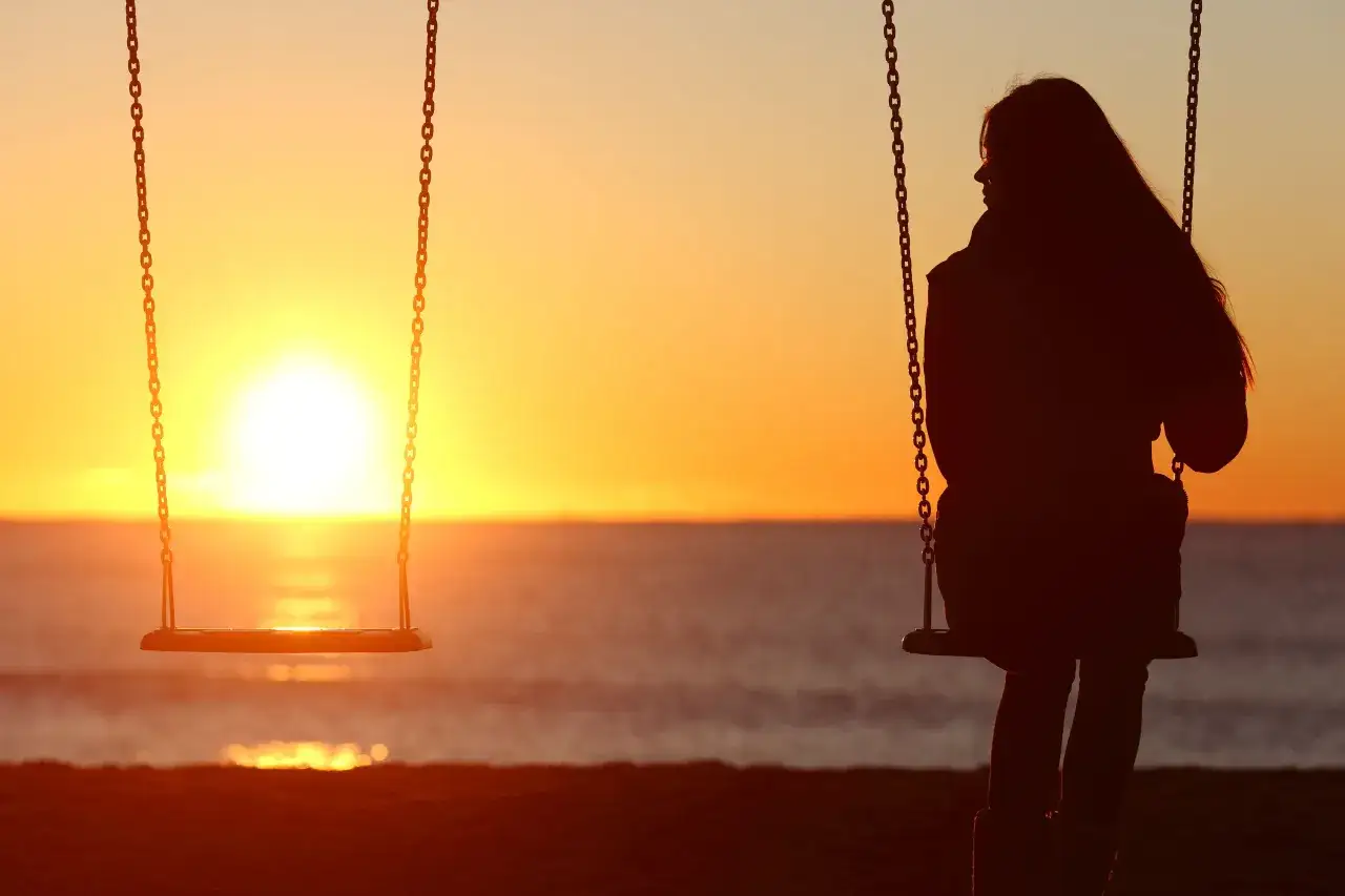 Silhouette di una ragazza su un'altalena al tramonto, con un'altra altalena vuota accanto. Un'immagine che evoca amicizie che finiscono nel silenzio.