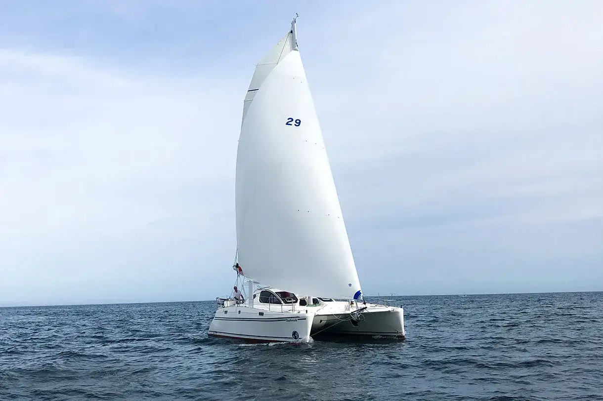 Catamarano con grande gennaker avvolgibile spiegato, naviga su mare calmo sotto un cielo nuvoloso.