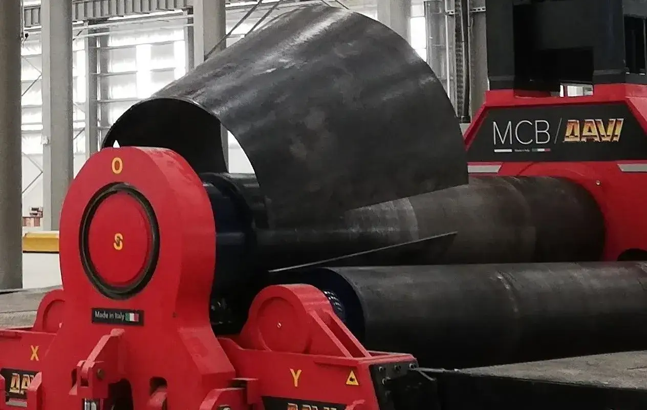 Maszyna do walcowania blachy formuje metalowy arkusz w kształt cylindra. Czerwone elementy maszyny i czarny, zakrzywiony metal.