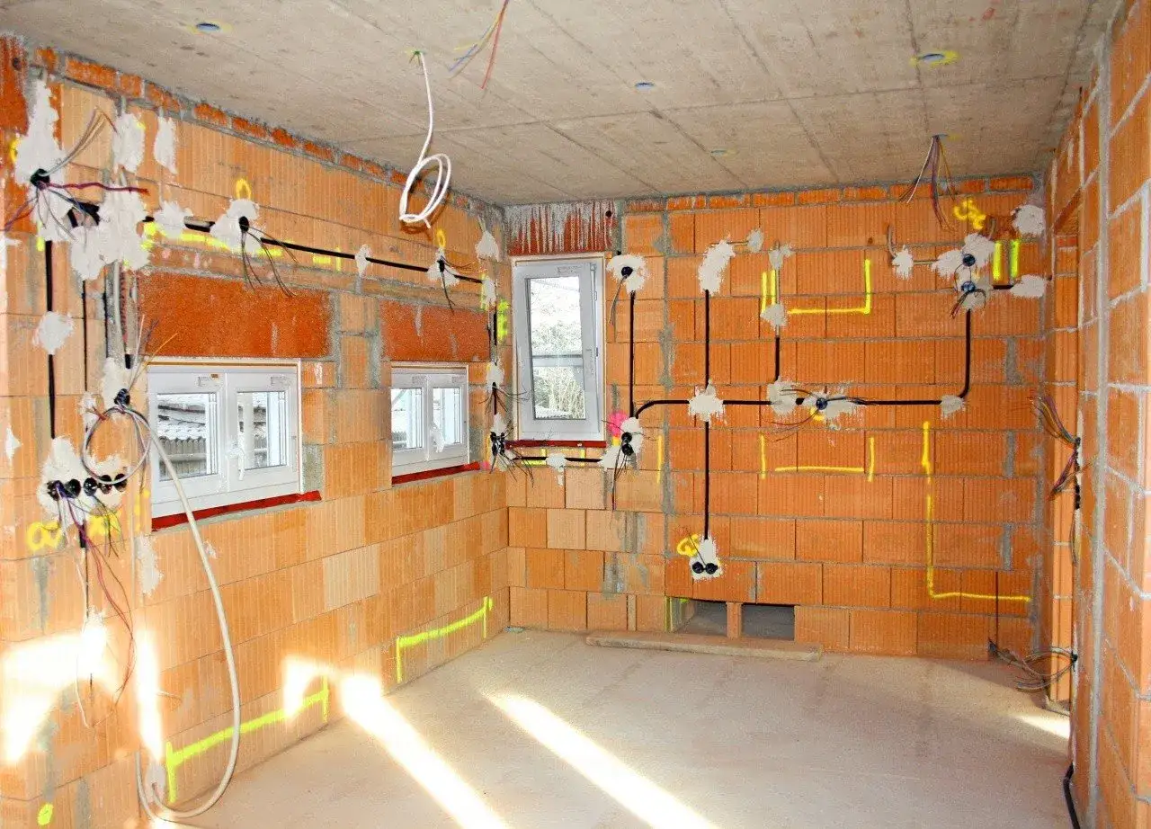 Rozprowadzona instalacja elektryczna w nowym budynku z cegły. Widoczne przewody, puszki i oznaczenia na ścianach.