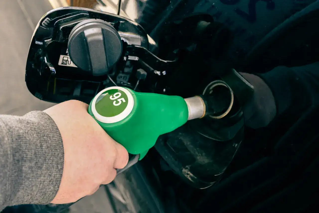 Mano sujetando una manguera de gasolina verde con el n&uacute;mero 95 en un c&iacute;rculo verde. El coche se est&aacute; repostando. Sin plomo 95 es gasolina.