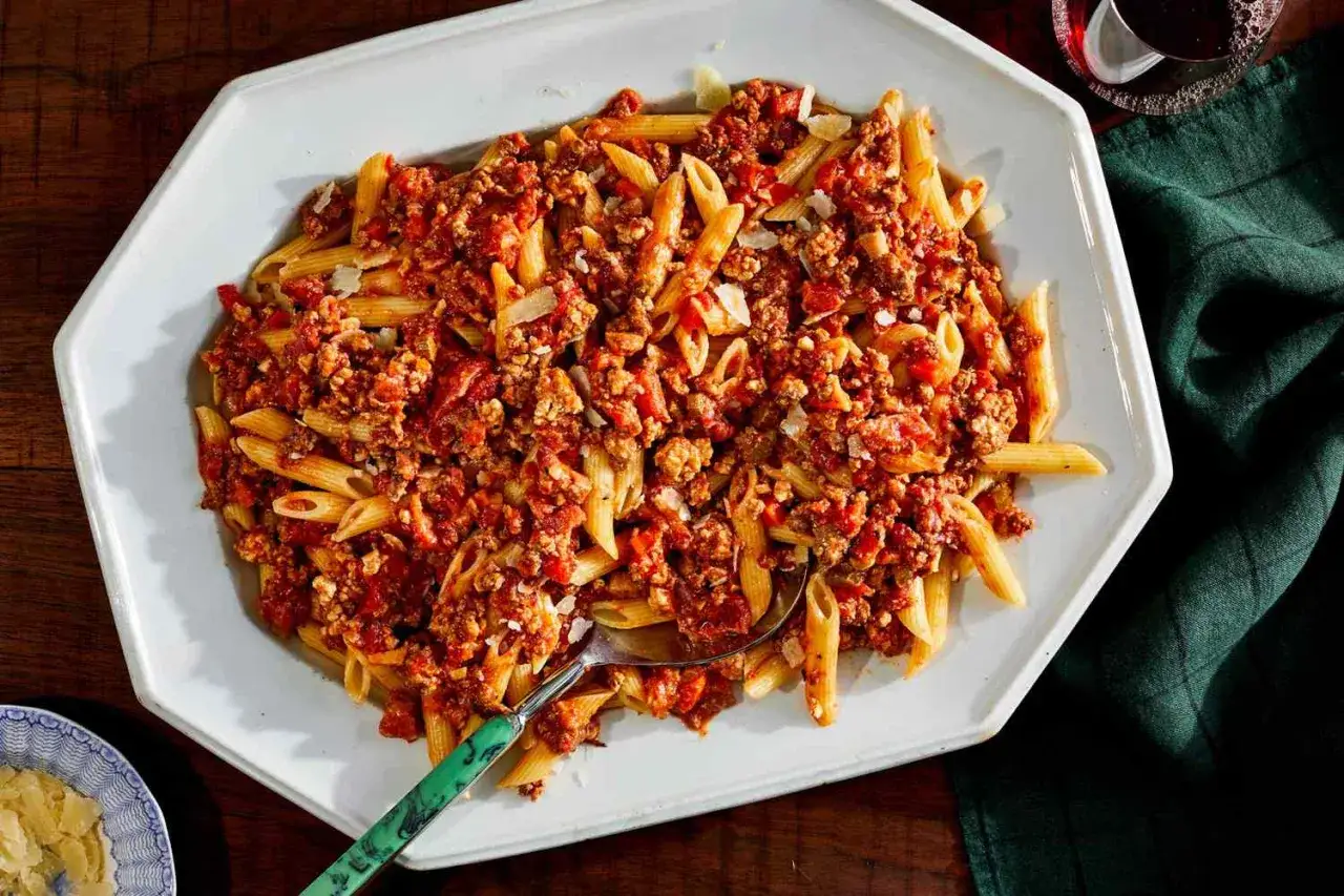 Un plato generoso de macarrones a la boloñesa, con abundante salsa de carne y tomate, espolvoreado con queso rallado.