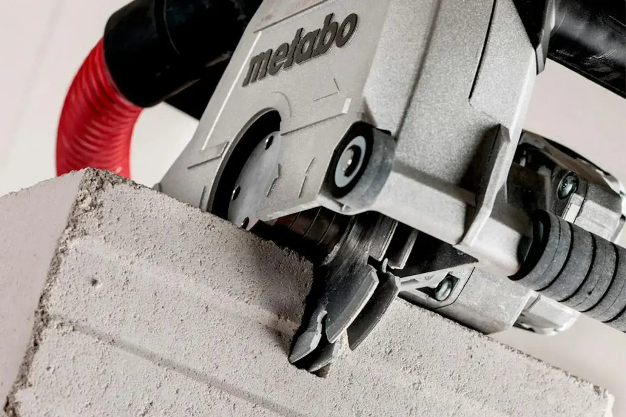 Metabo-maskin som skapar ett spår i betong. En röd slang ansluten för dammutsug.