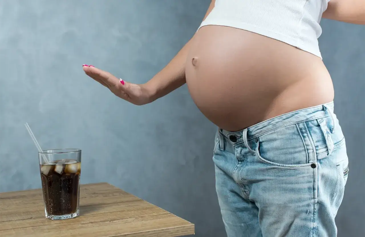 Schwanger und verzichtet auf Cola. Eine Hand weist eine Cola mit Eisw&uuml;rfeln und Strohhalm ab.
