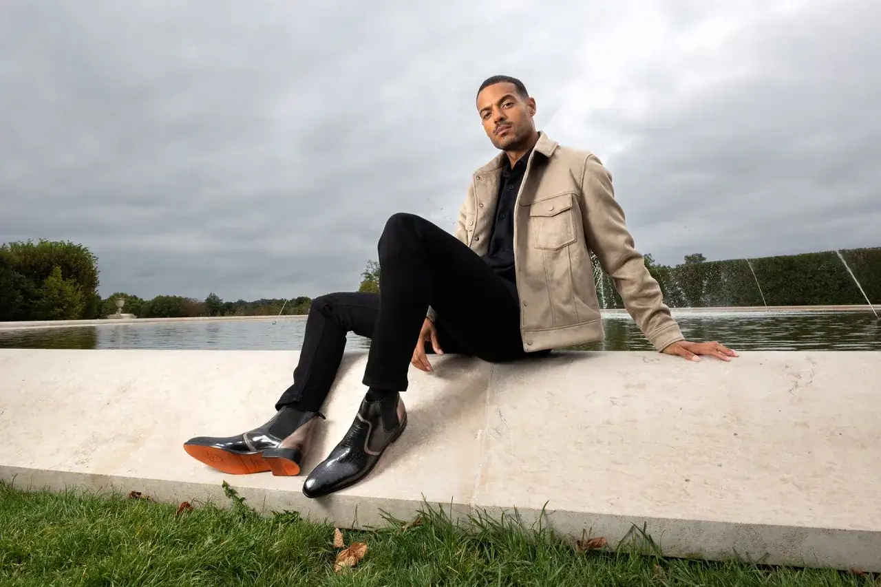 Un homme pose près d'une fontaine, vêtu d'un pantalon noir et de bottines homme élégantes.