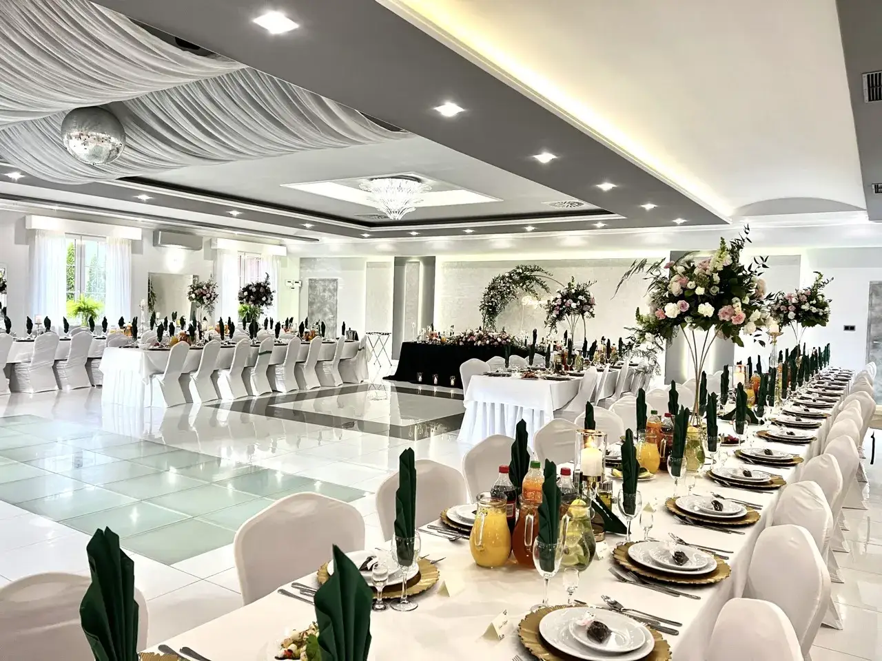 Elegancka sala weselna z białymi pokrowcami na krzesłach i ozdobnymi kwiatami. 