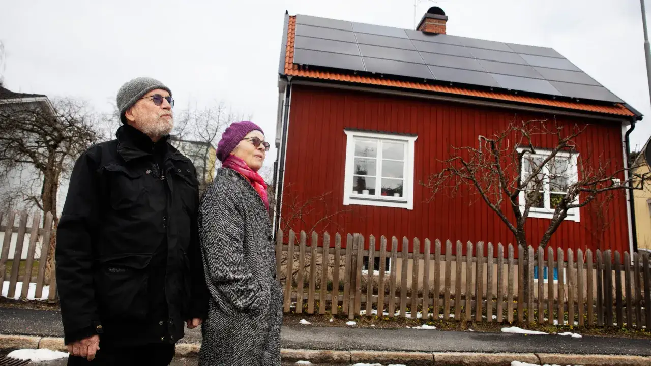 Ett par tittar upp mot taket p&aring; sitt r&ouml;da hus, t&auml;ckt av stilrena longi 410w full black solpaneler.
