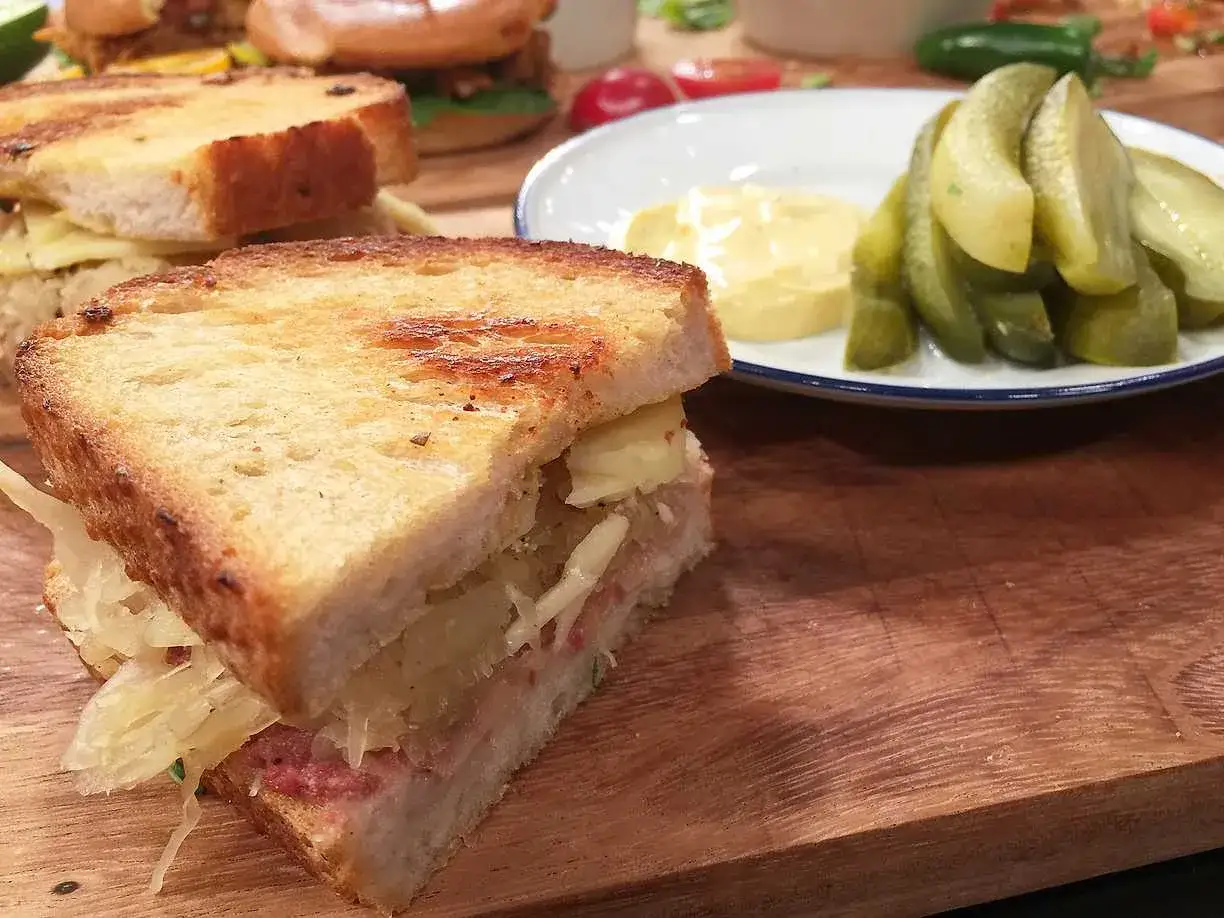 En saftig reuben sandwich med krispigt br&ouml;d, syrad k&aring;l och ost. Serveras med dillpickles och senap.