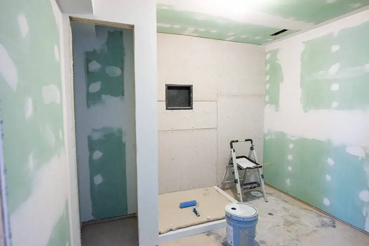 Bagno in fase di ristrutturazione con pareti in cartongesso pronte per le piastrelle. Si intravede una nicchia e attrezzi da lavoro.