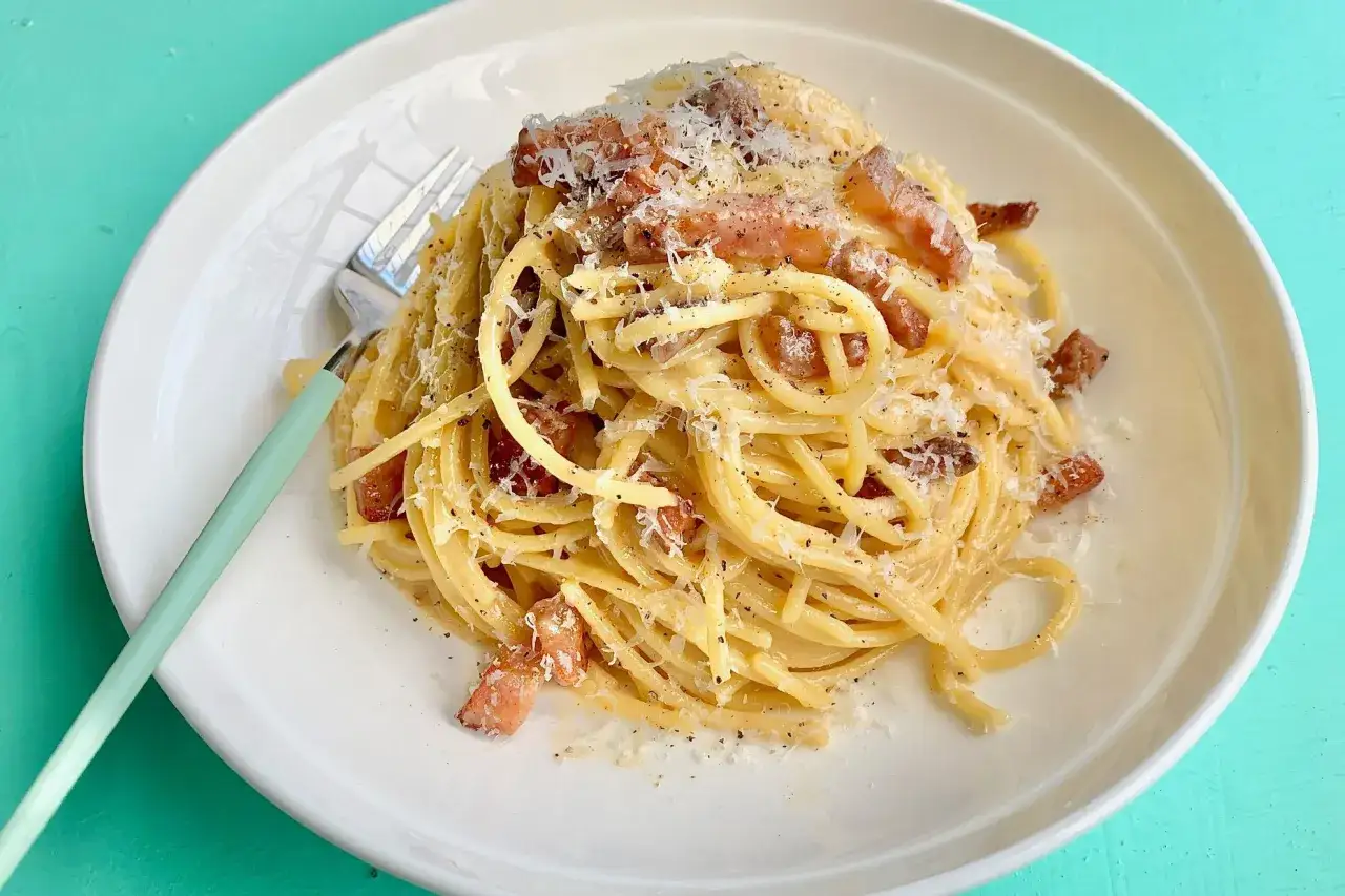 Une assiette de p&acirc;tes carbonara cr&eacute;meuses, garnie de lardons croustillants et de parmesan r&acirc;p&eacute;, avec une fourchette &agrave; la menthe.