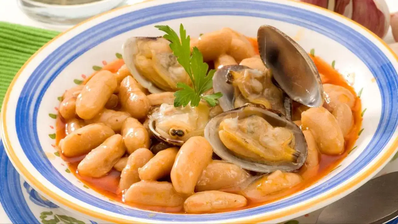 Plato de fabes con almejas, un guiso tradicional asturiano. Las jud&iacute;as blancas est&aacute;n tiernas y jugosas, acompa&ntilde;adas de almejas frescas y un toque de perejil.