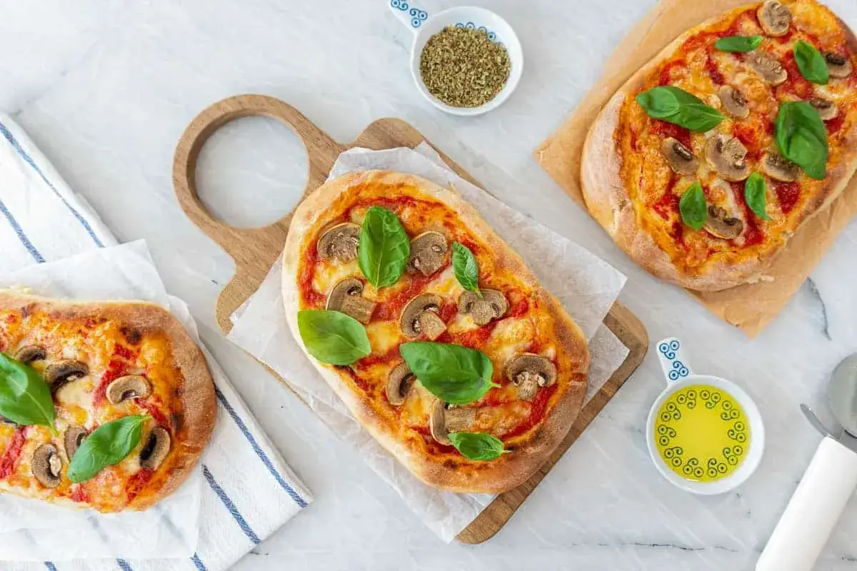 Trois pinsas appétissantes garnies de champignons, de fromage et de basilic. Une recette de pinsa facile à réaliser pour un repas savoureux.