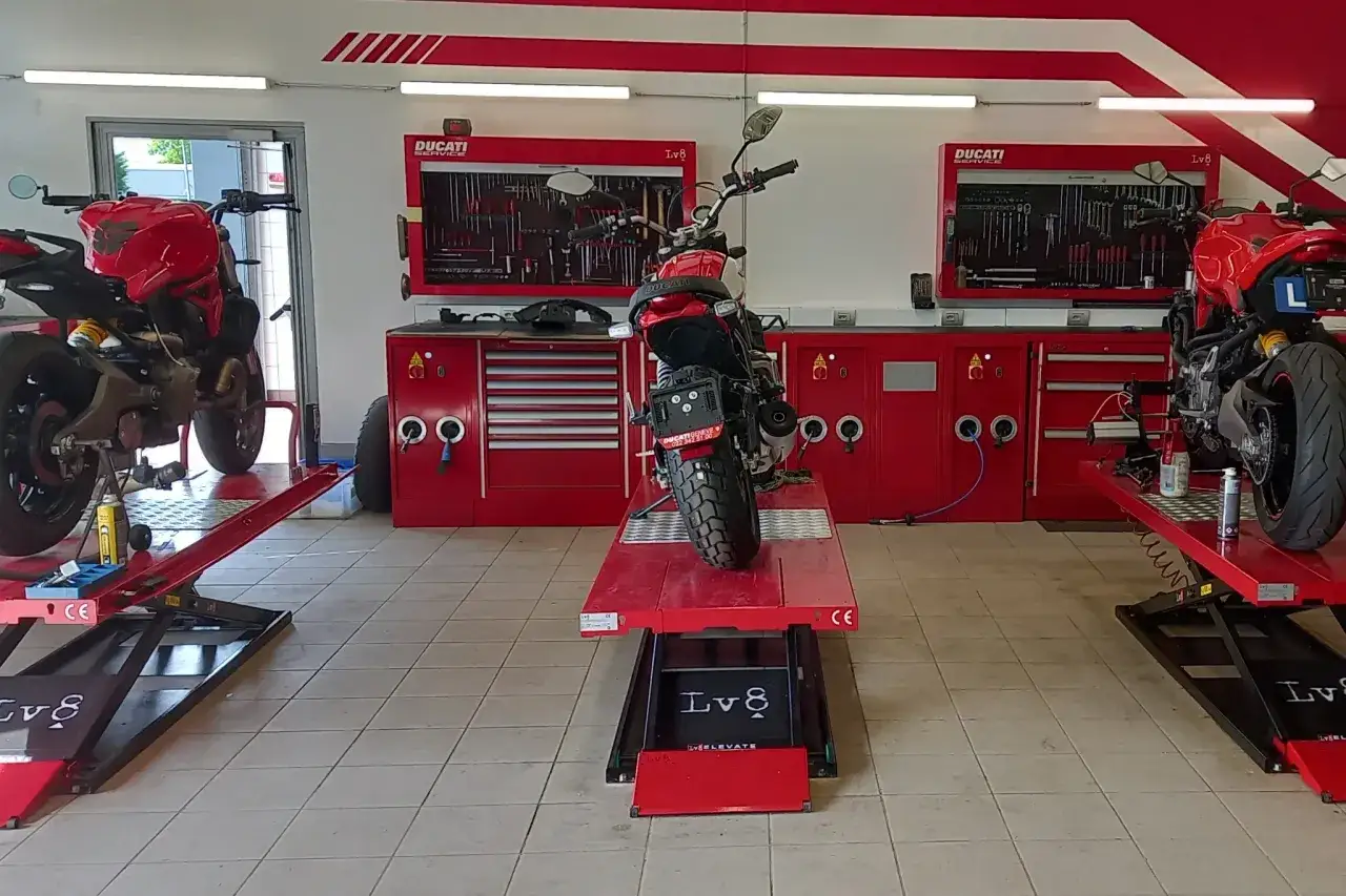 Un garage per moto fai da te con sollevatori rossi e moto Ducati. Attrezzi organizzati su pannelli a muro.