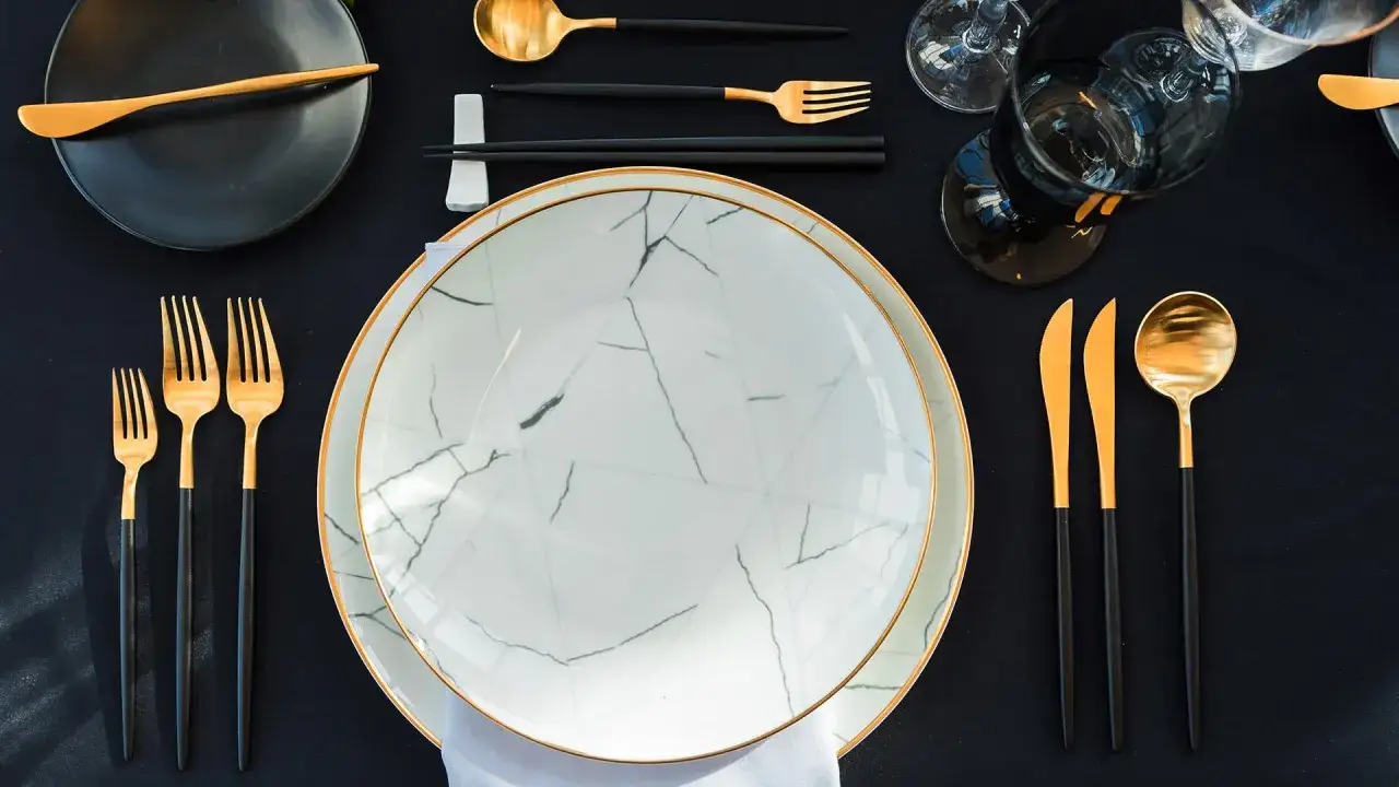Service à la française définition : une table élégante avec des assiettes marbrées, des couverts dorés et noirs, et des verres sombres.