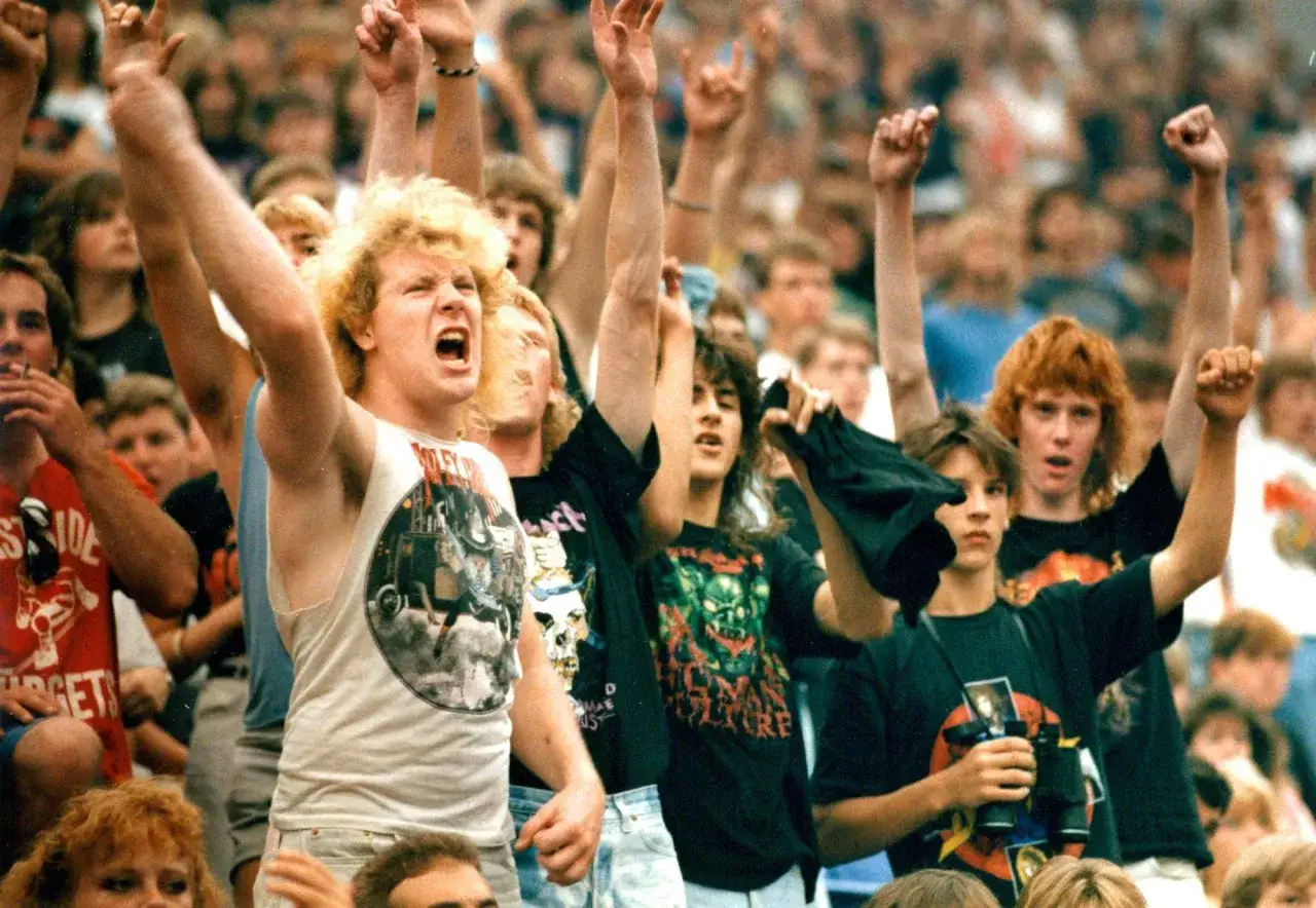 Fans jubeln bei einem Konzert der **metal bands 80er**. Sie tragen Band-T-Shirts und machen das 