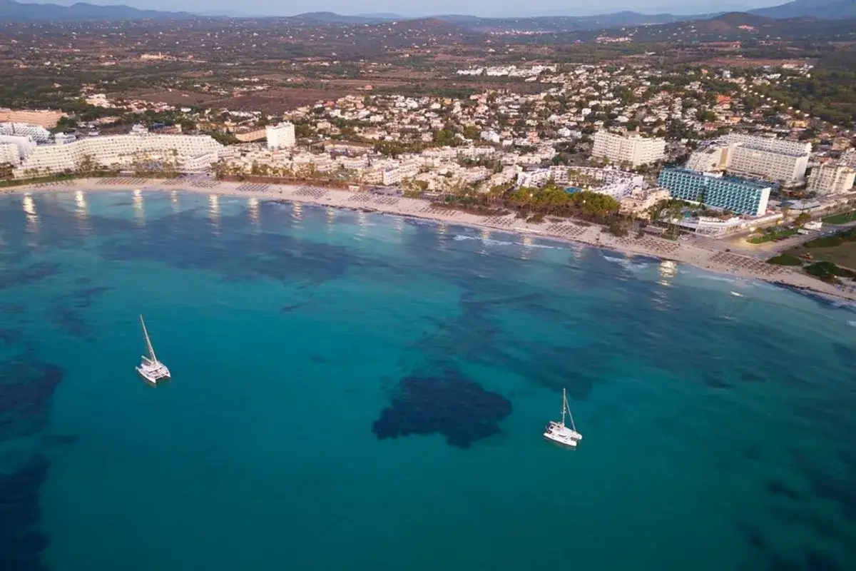 Traumhafte Bucht mit zwei Katamaranen vor der K&uuml;ste von Sa Coma. Die Altstadt und Hotels s&auml;umen den Strand.