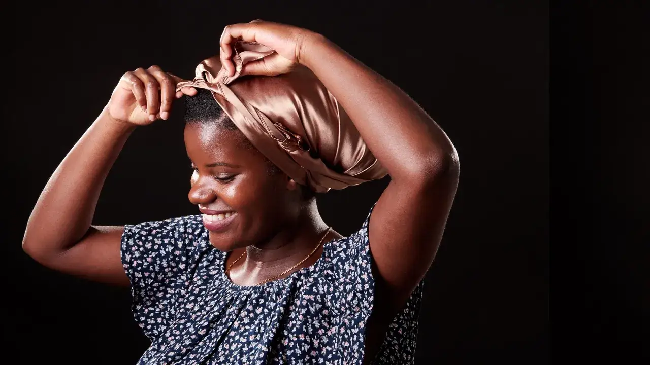 Une femme ajuste son foulard en satin, une coiffure protectrice nuit id&eacute;ale pour pr&eacute;server ses cheveux.