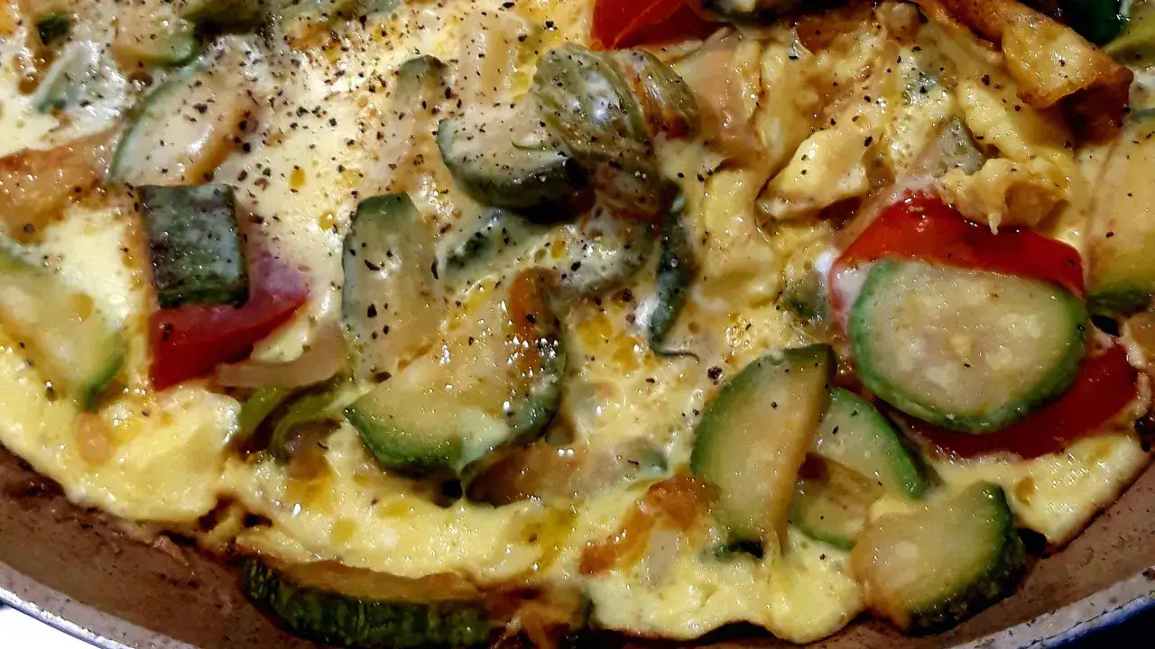 Frittata aux l&eacute;gumes, un plat color&eacute; avec des courgettes, des tomates et des poivrons, saupoudr&eacute; de poivre noir.