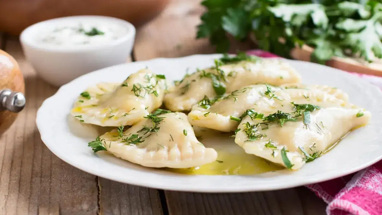 Leckere Pierogi Ruskie, garniert mit Dill und Butter, serviert auf einem Teller mit einem Schälchen Dip.