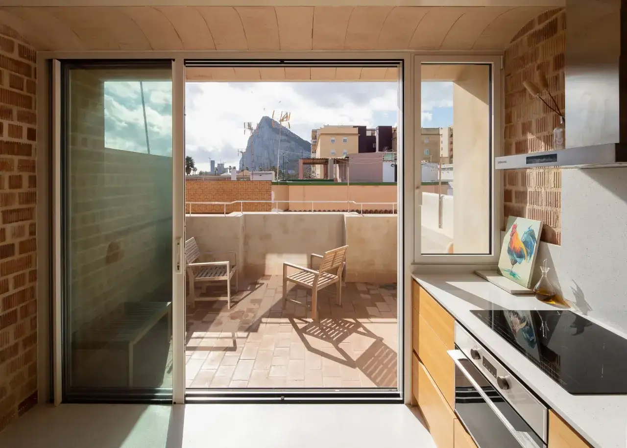 Cocina moderna con encimera de cuarzo y **ventanas aislantes** que dan a una terraza con vistas a un pe&ntilde;&oacute;n.