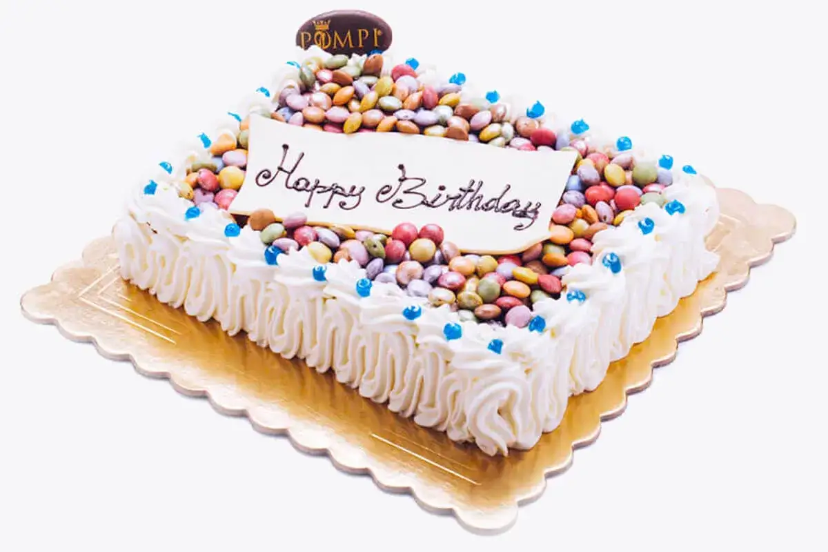 Torta per bambini con glassa bianca, caramelle colorate e scritta
