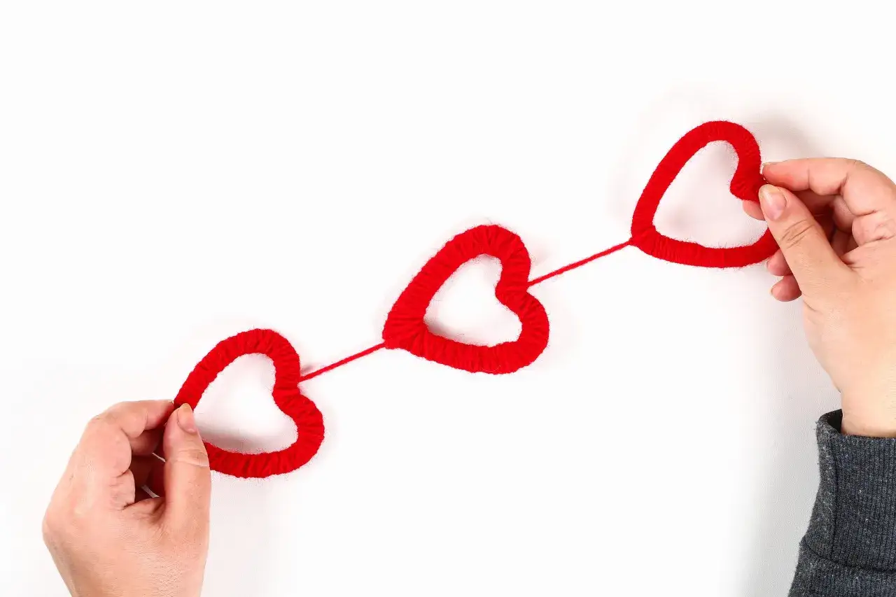 Mani che creano cuori rossi con lana, perfetti per san valentino lavoretti fai da te.