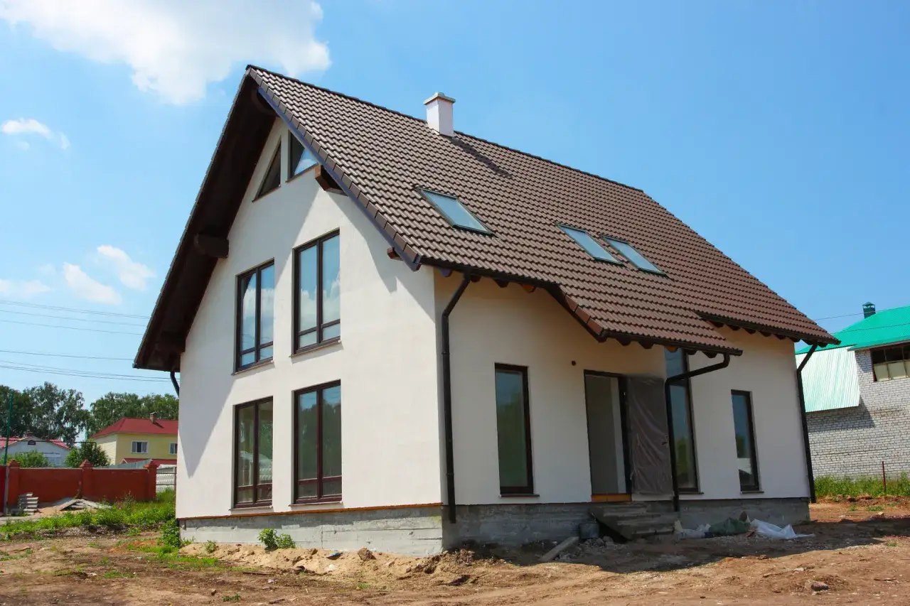 Nowy dom w budowie, z brązowym dachem i białymi ścianami. Warto pomyśleć o energooszczędności, by obniżyć przyszłe ceny energii.