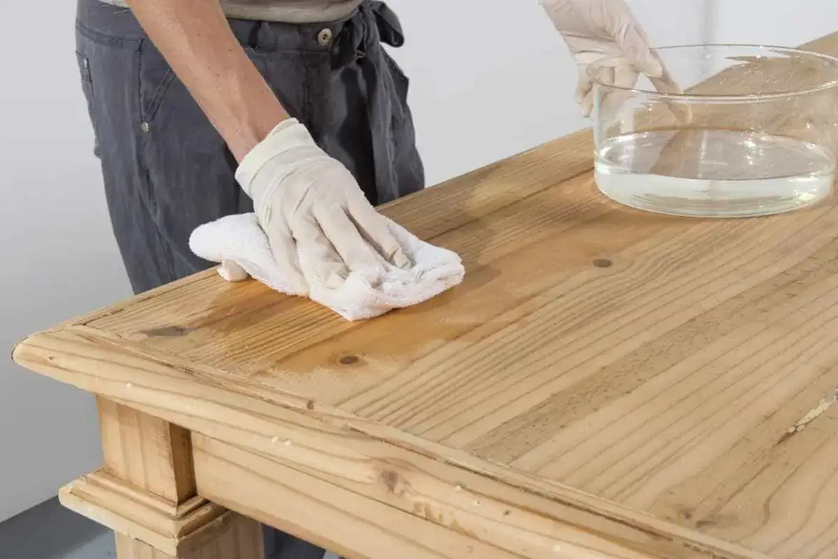 Person mit Handschuhen wischt mit einem Tuch &uuml;ber einen Holztisch, um ihn f&uuml;r das tisch lackieren vorzubereiten.