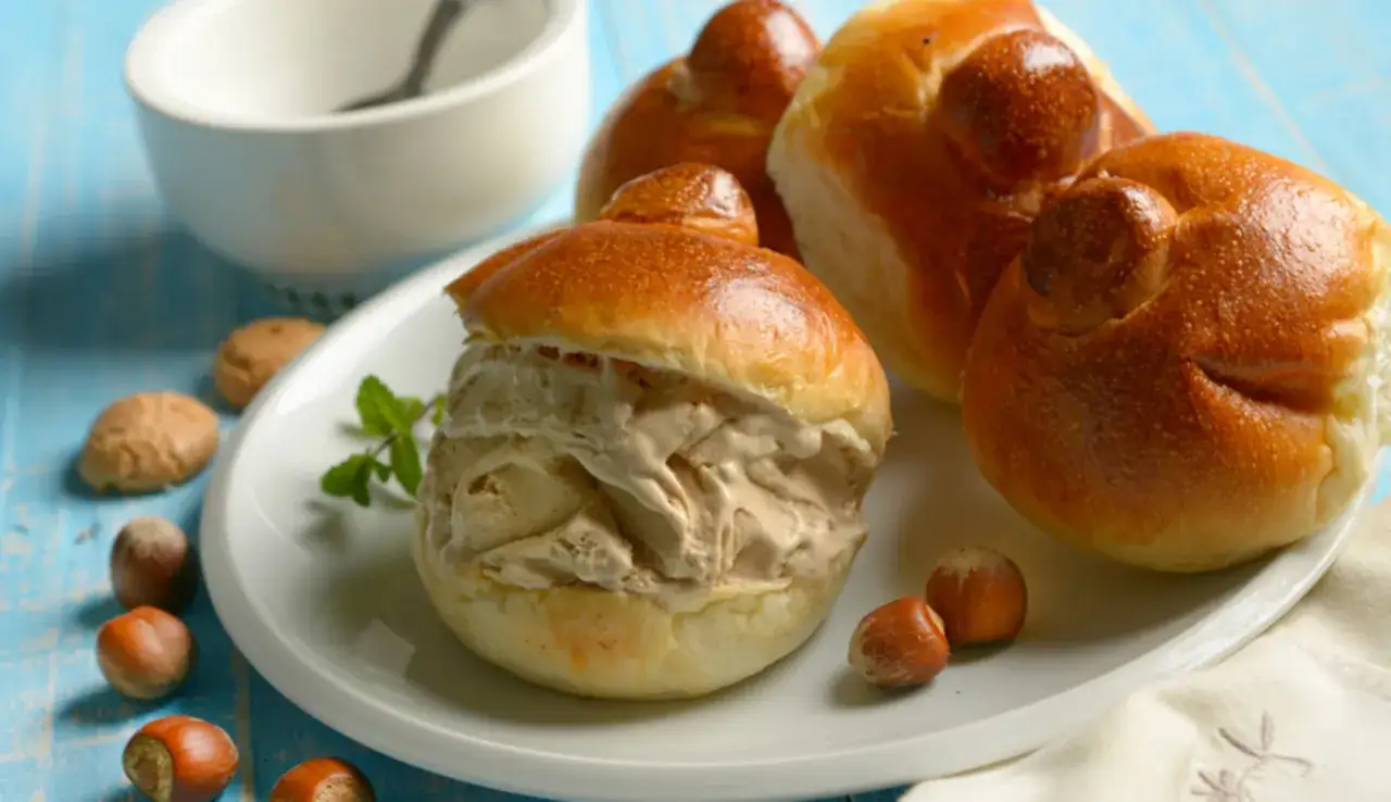 Brioche col tuppo ripieno di gelato, con nocciole e biscotti intorno.