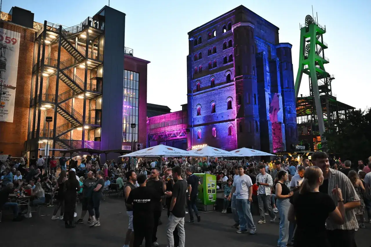 Menschen feiern auf einem Industriegelände, beleuchtet von bunten Lichtern. Ein lebendiges Fest an besonderen **Extraschicht Spielorten**.