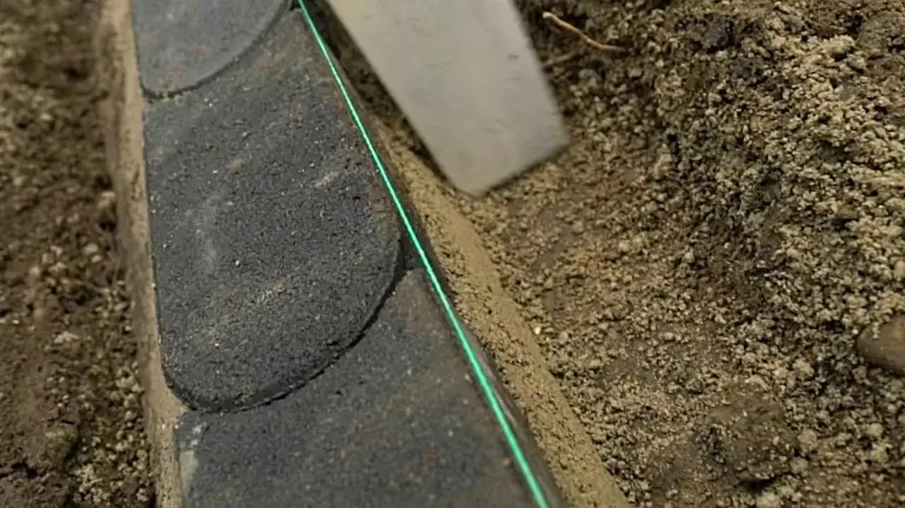 Układanie obrzeży trawnikowych z kostki betonowej. Zielona nić wyznacza idealną linię.