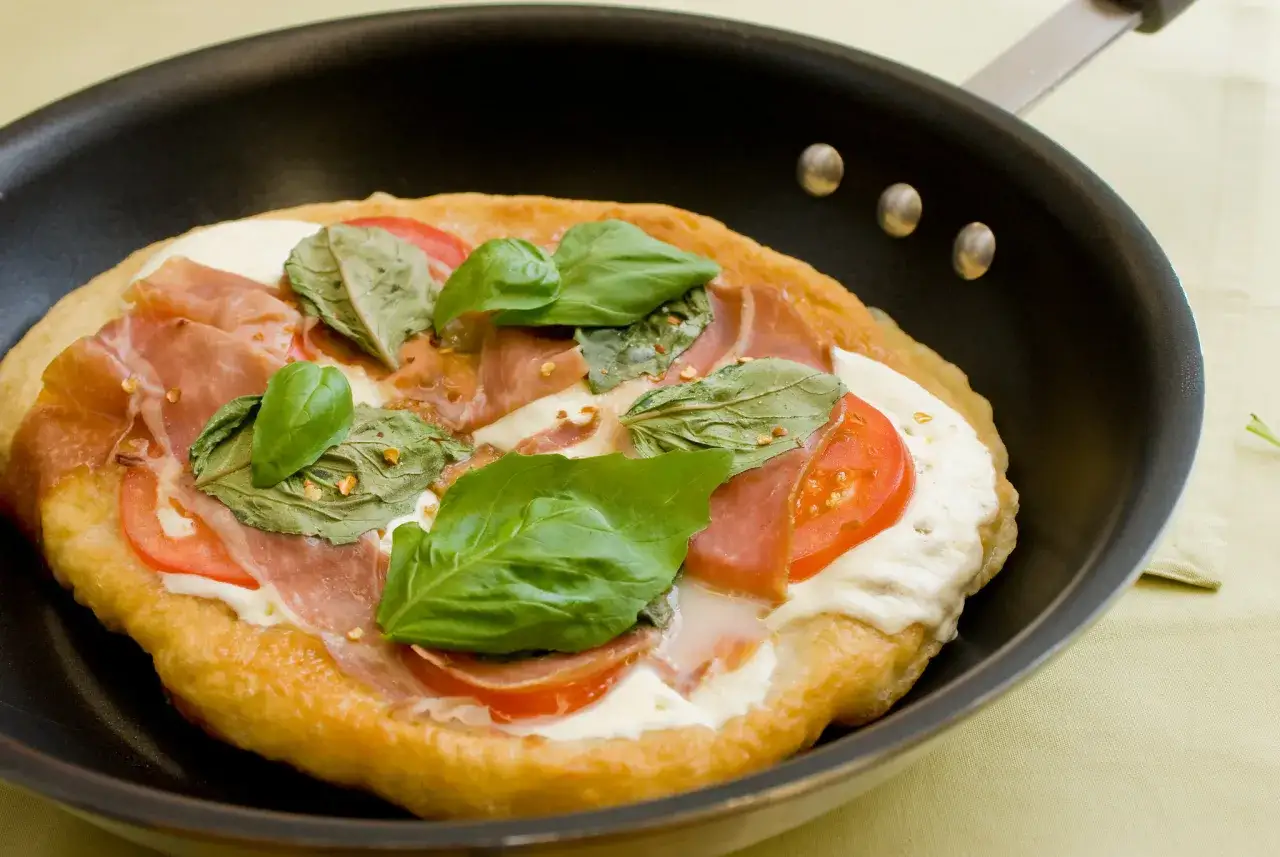 Pyszna pizza z patelni z szynką parmeńską, pomidorami i bazylią, gotowa do podania.