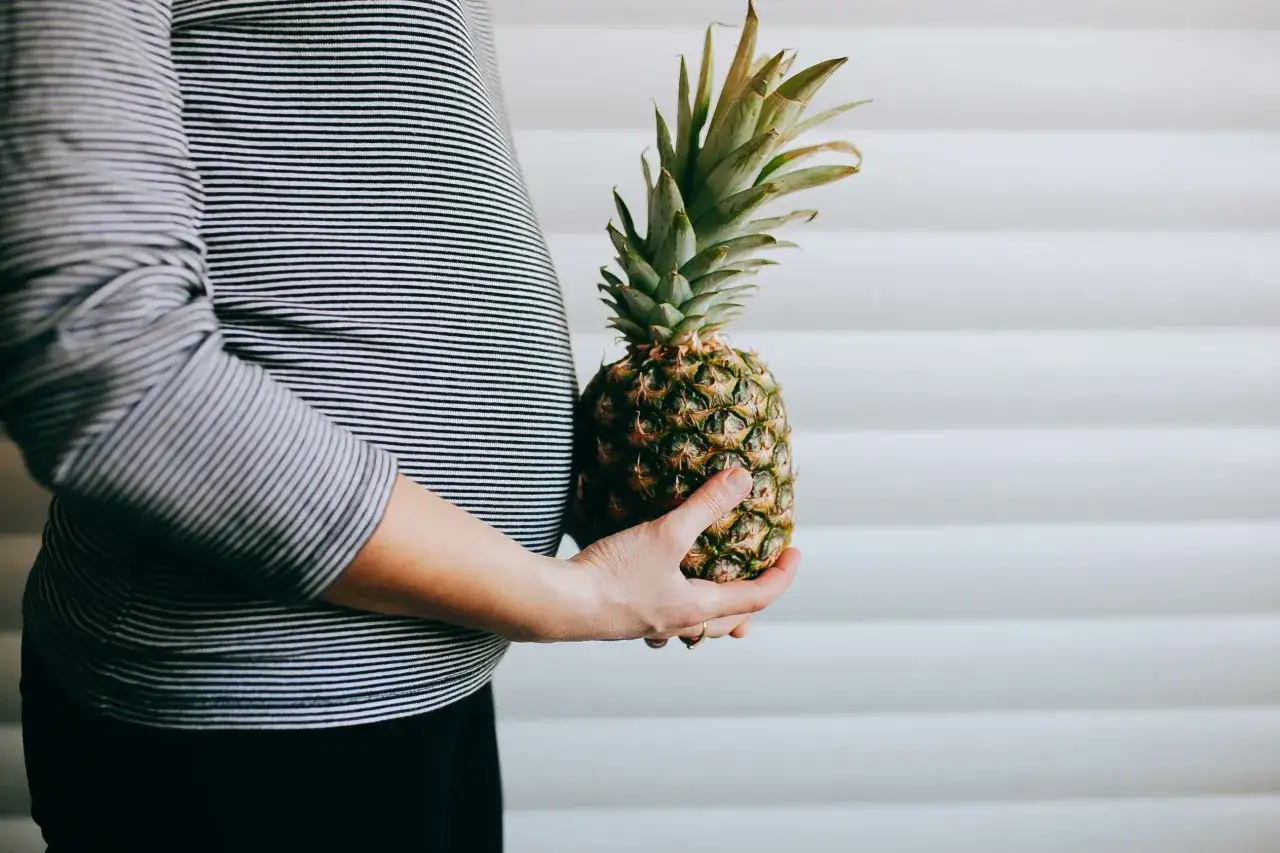 Brzuch kobiety w paski obejmuje ananas.