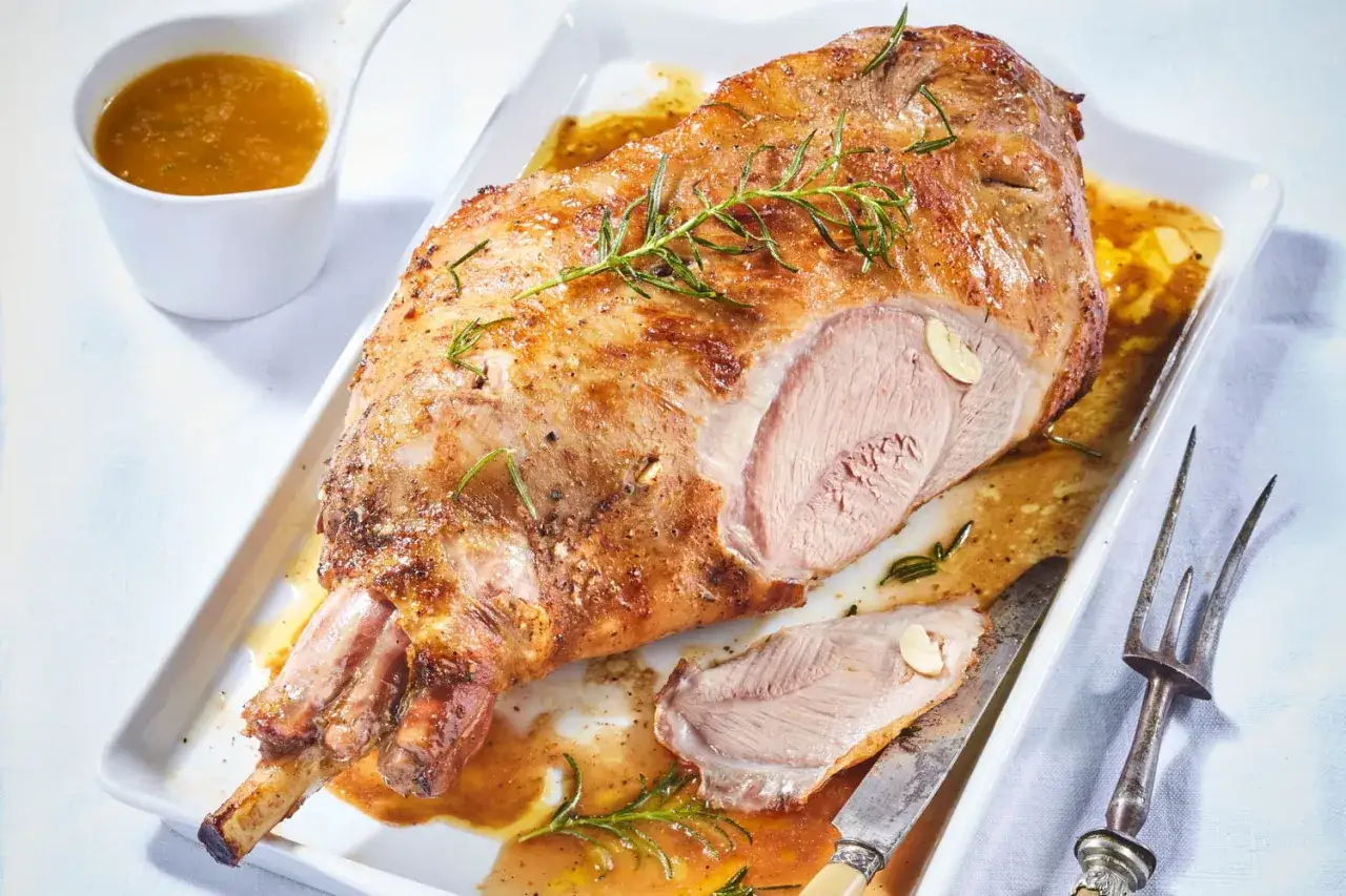 Gigot d'agneau rôti, doré et juteux, garni de romarin frais. Un délice pour la cuisson parfaite.