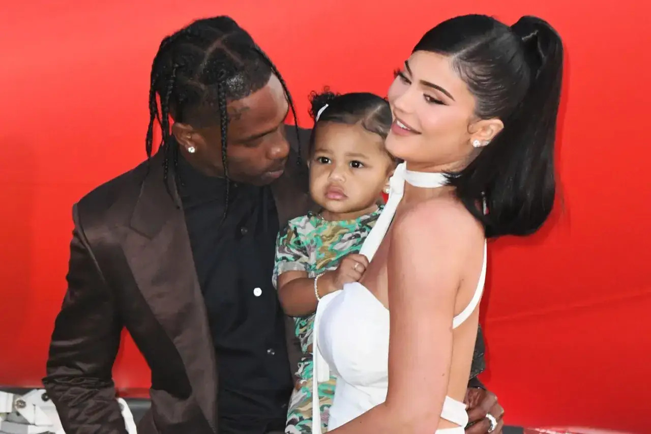 Travis Scott z dziećmi, córką Stormi i Kylie Jenner, na czerwonym tle.