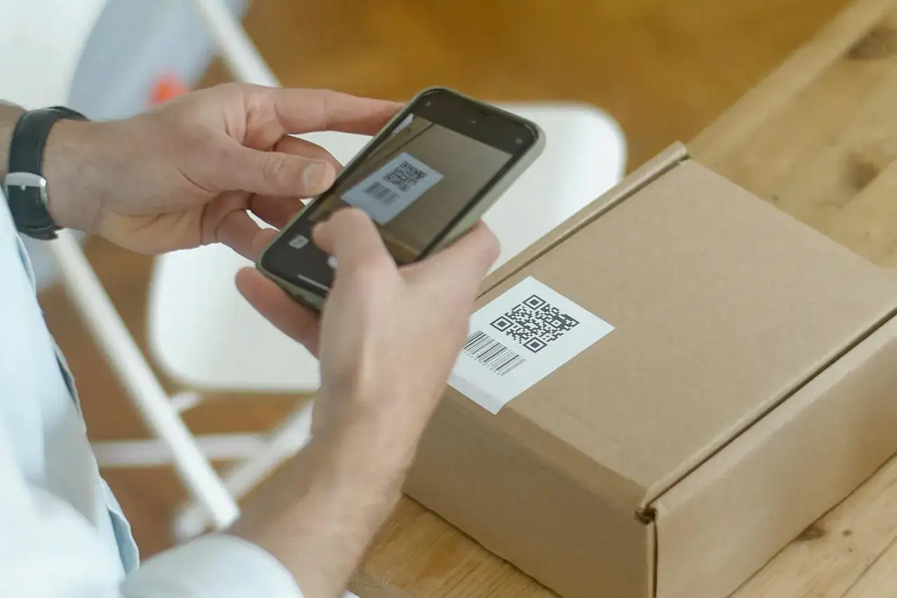 Ręce trzymają smartfon, którym skanują kod QR na paczce. Tak właśnie można zrobić skanowanie kodu.
