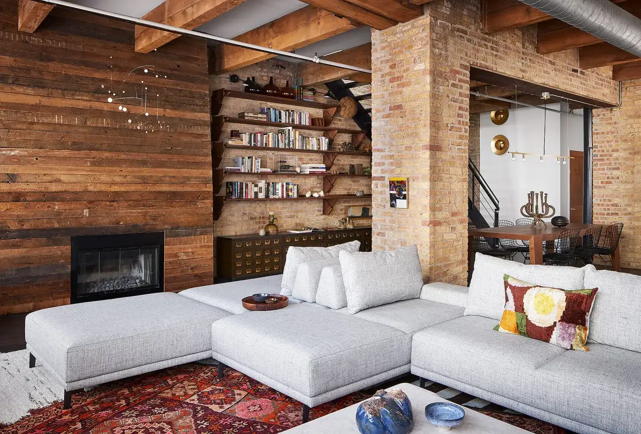 Gem&uuml;tliches Industrie Loft mit Holzw&auml;nden, Kamin, B&uuml;cherregalen und einer gro&szlig;en Couch.