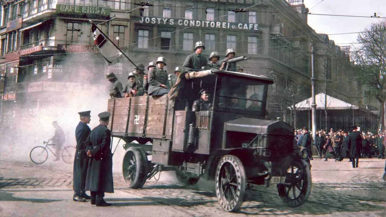 Militär auf einem LKW mit Hakenkreuzflagge, ein Symbol für das Scheitern der Weimarer Republik. Polizisten beobachten die Szene.