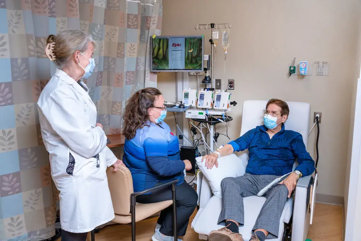 Pacjent podczas chemioterapii, otoczony opieką lekarki i pielęgniarki. W tle aparatura medyczna.
