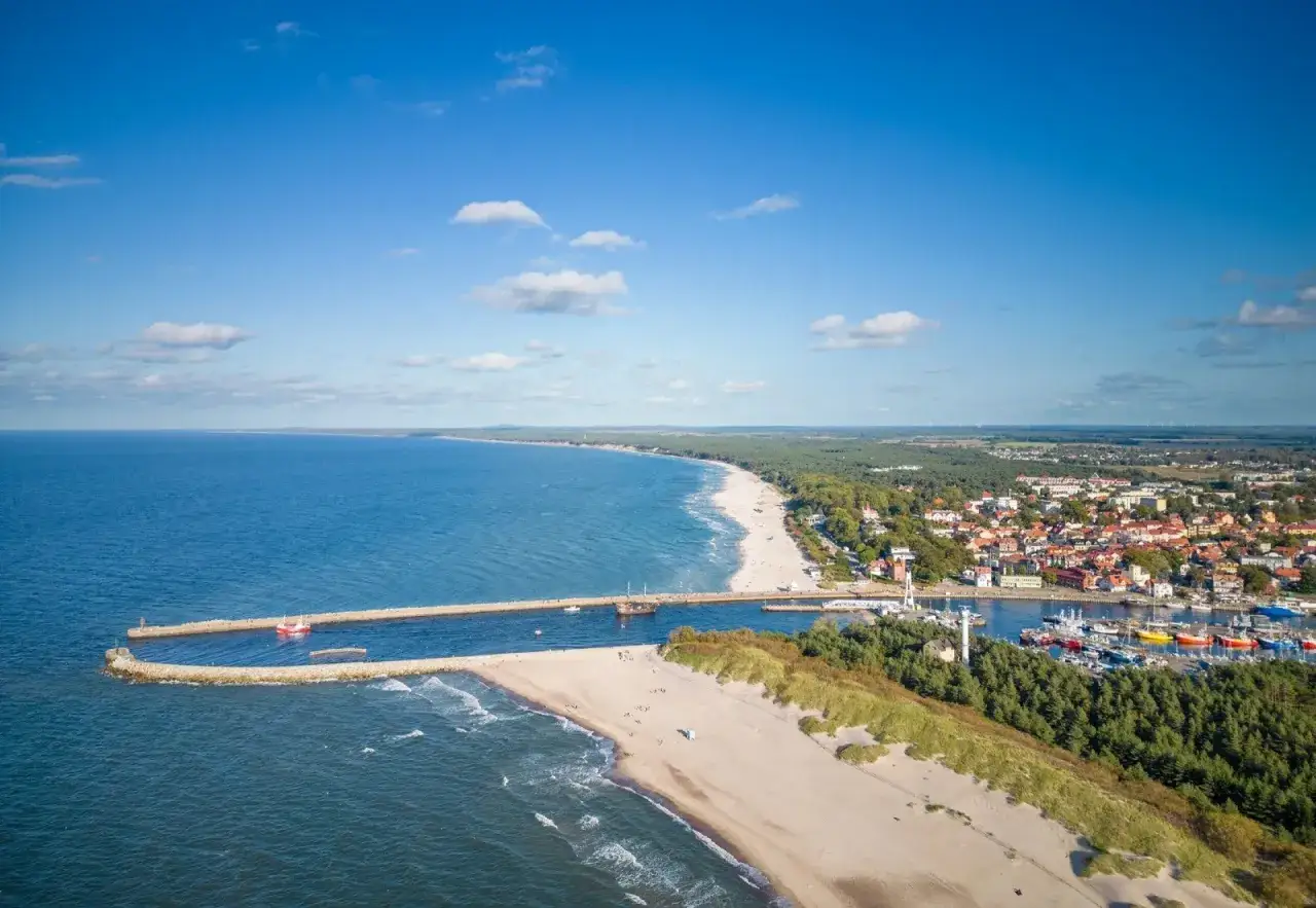 Widok na port i plażę w Ustce. Widać falochrony, łodzie, budynki i las. To idealne ustka atrakcje turystyczne.